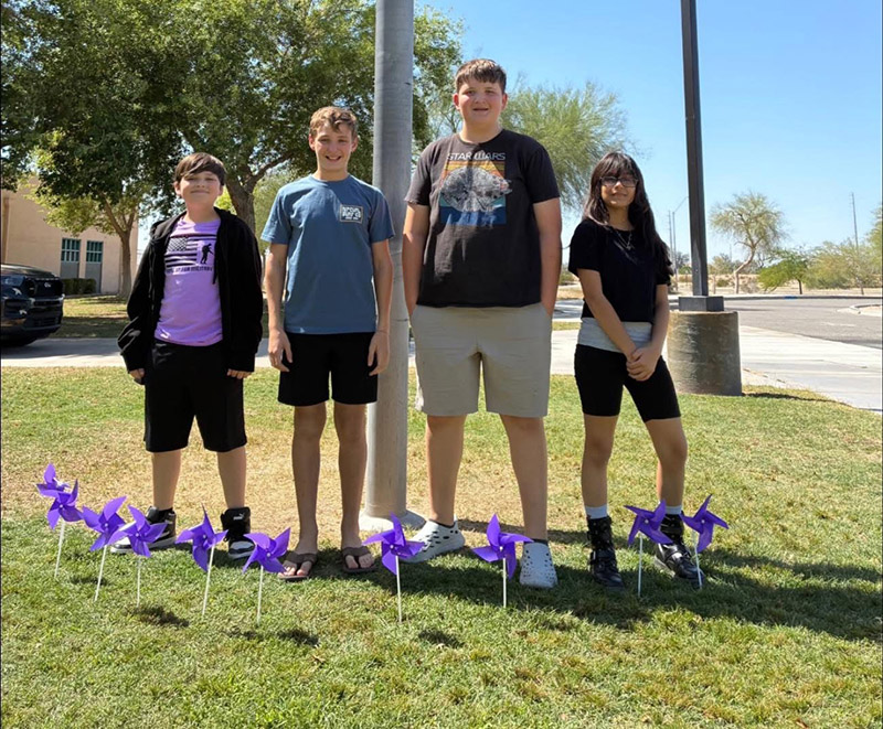 Group of four students outside behind purple pinwheels