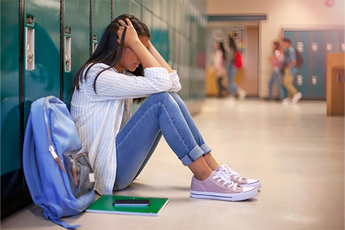 Frustrated teenage female student sitting with head in her hands in the school hallway