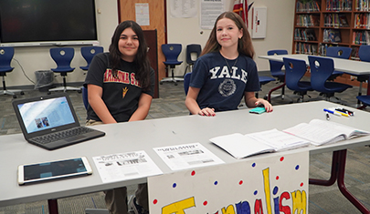 Two happy sixth grade students sitting behind a college prep information table