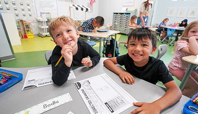 Two happy elementary school boys looking up from their desk in the classroom