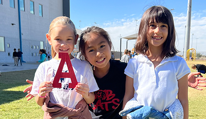 Three happy elementary school girls outside on campus holding up a big letter A