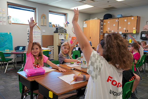 Students in a classroom with their hands raised