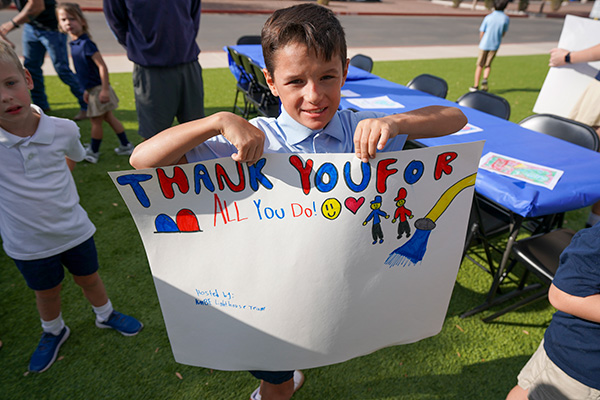 A little boy holding his handmade poster that says, "Thank you for all you do!"