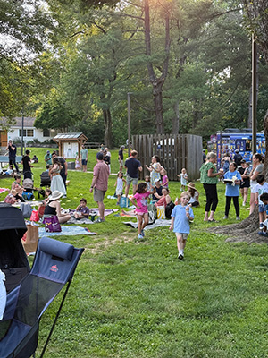 Children and their parents sitting on the ground or standing while they eat and visit with each other at the end-of-year picnic