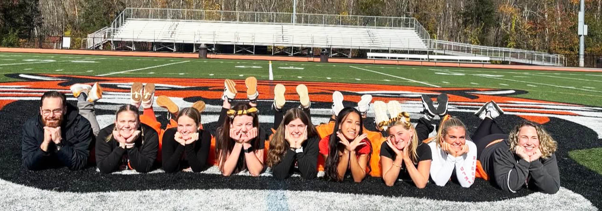 Group of happy students and staff posing for a fun picture on the football field