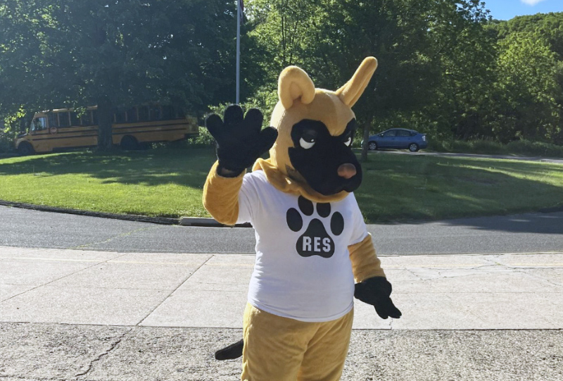 Loyal mascot, Rex, waving to the camera outside Ridgebury Elementary campus