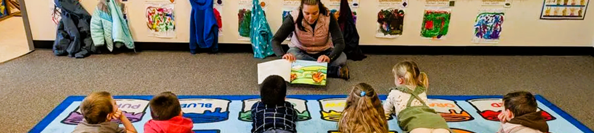 headerphoto_AboutUs Students listening to an adult read a book