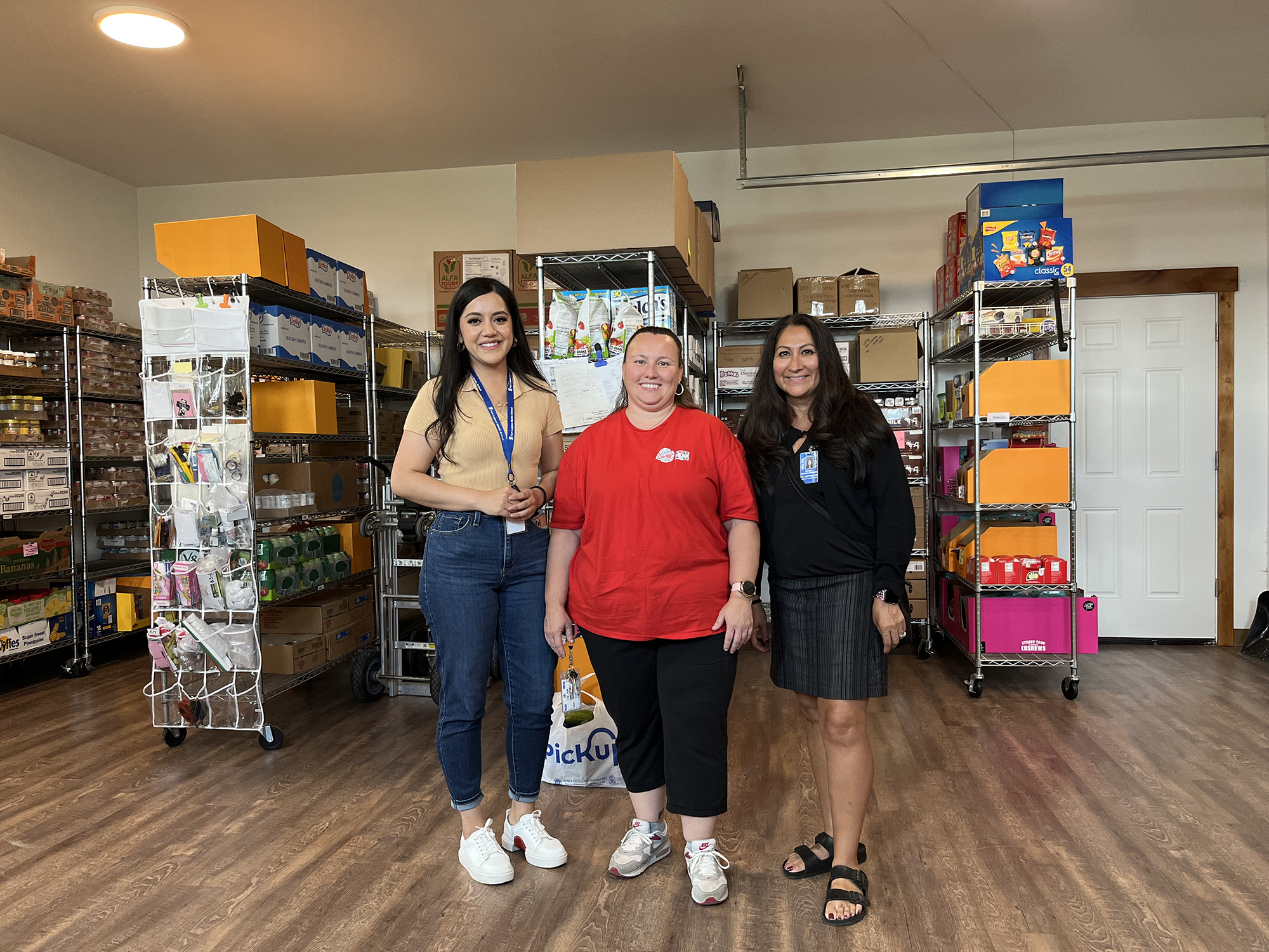 Three ladies in front of storage units of food items