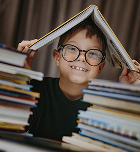 Happy school boy hiding in between books