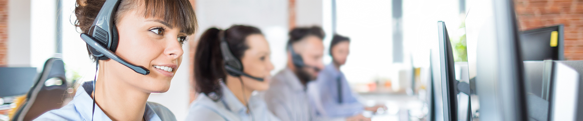 four people with headsets sitting in front of computers