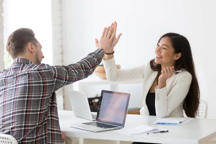 Young asian and caucasian partners giving high five at workplace