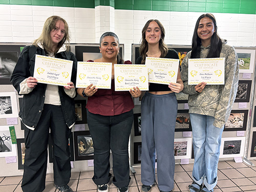 Four students holding up art show certificates for their artwork