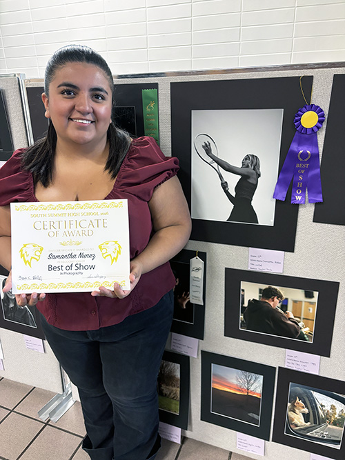Art show winner holding certificate in front of artwork