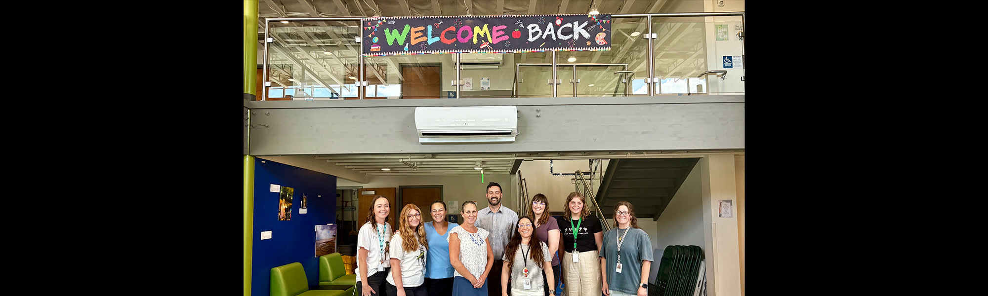 Happy staff members posing for a picture under a welcome back banner in the school lobby