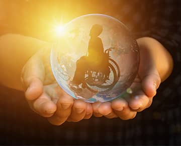 hands holding a globe with a person in a wheelchair in the center of it