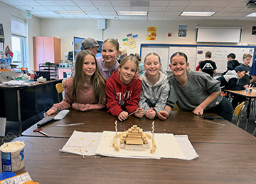 sidebargraphic_AboutUs Group of happy girls next to their projects in the classroom