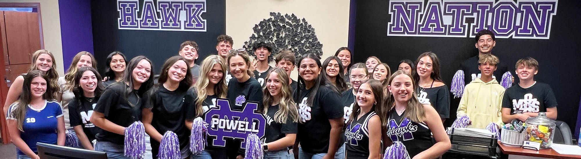 Group of happy students and cheerleaders under a Hawk Nation sign