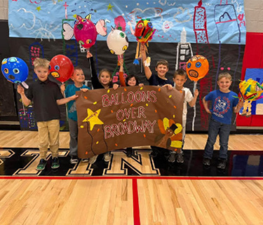 students holding decorated balloons over a sign that reads Balloons Over Broadway