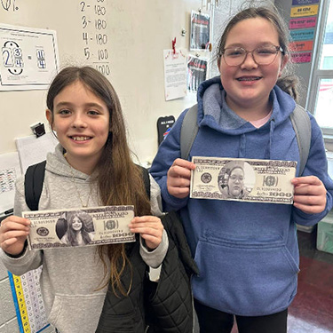 two students holding up fake dollars with their pictures on them