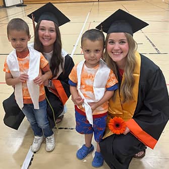 two graduating students next to youngsters