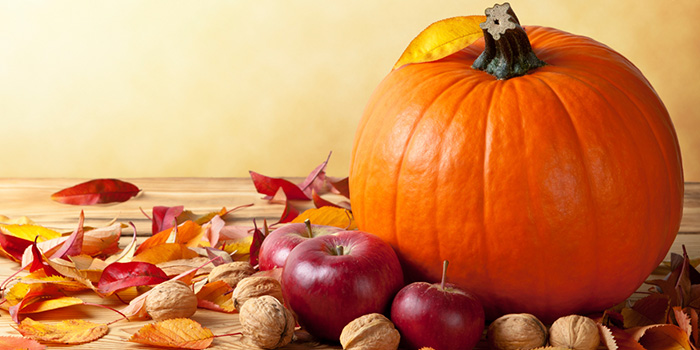 Big pumpkin next to apples, nuts, and leaves