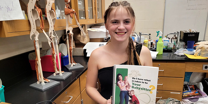 Student holding a "Do I Have What it Takes to be Your Babysitter?" manual