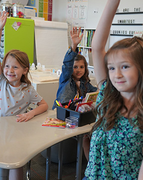 Three girls raising their hands in the classroom