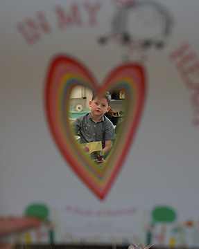 A student peeking through a heart-shape in a book