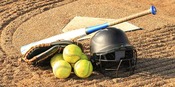 Baseball helmet, bat, and balls on sand beside a base