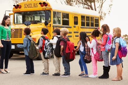 kids with backpacks lined up to get on a yellow school bus