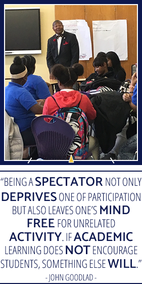 Teacher in classroom with students in class with "Being a spectator not only deprives one of participation but also leaves one's mind free for unrelated activity. If academic learning does not encourage students, something else will." - John Goodlad quote