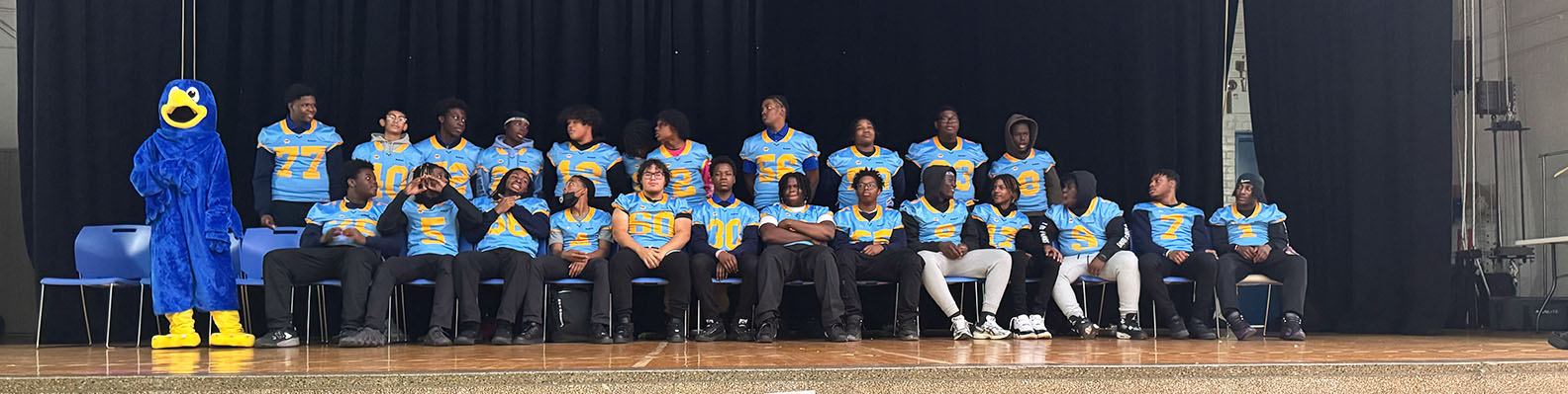 Group of students in football jerseys on stage with school mascot