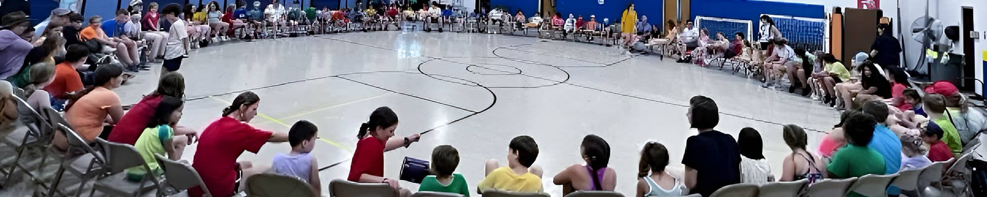large group of students sitting in chairs in a circle around the gym