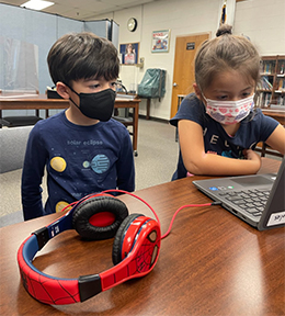 Two students with masks looking at a computer