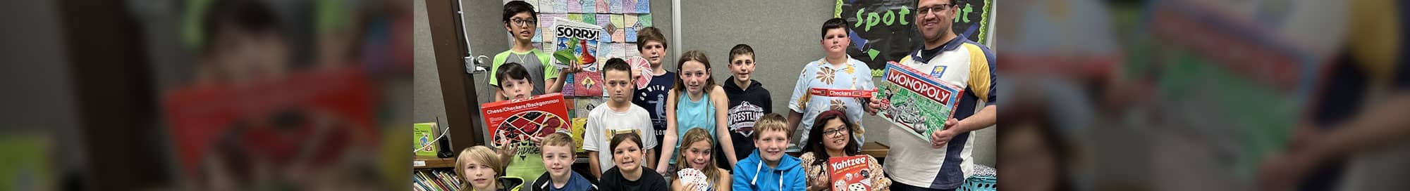 smiling group of students with a teacher holding up different board games