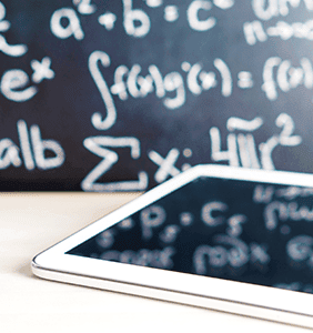 Ipad on a desk with a chalkboard with math equations in the background