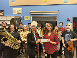 Dr. Martin is on the left presenting a check to Ms. Crust with members of the band in the back.