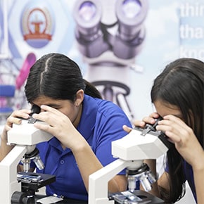 two students looking into microscopes with stem posters in the background