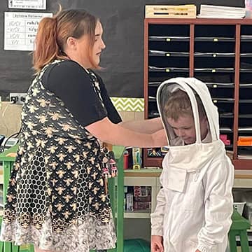 An adult helping a student put on a outfit to work with bees