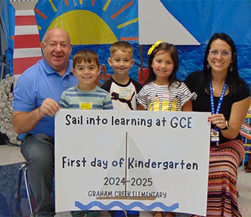 Students and teachers holding a sign saying First Day of Kindergarten