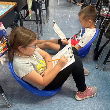 Two students sitting down and doing classwork