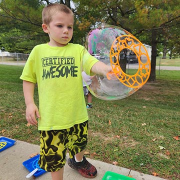 Boy using a wand to make a giant bubble outside