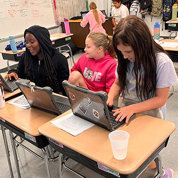 Three girls using laptops in class