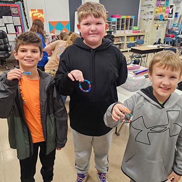 Three boys holding bracelet crafts