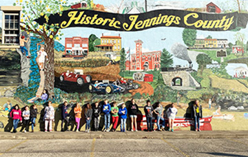 Students posing for a photo under a beautiful Historic Jennings County mural