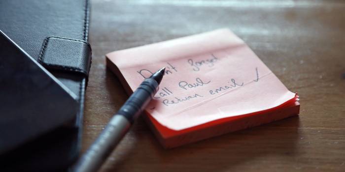 Sticky note pad with a reminder written on it and a pen beside it