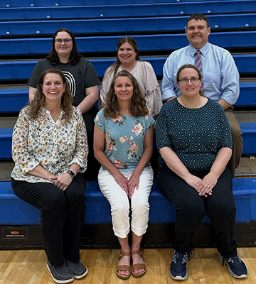 Group of six adults sitting on gym bleachers