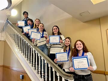 Students in a line on stairs holding awards