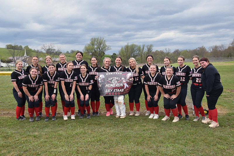 Softball team huddled around Lily Staab and her home run banner
