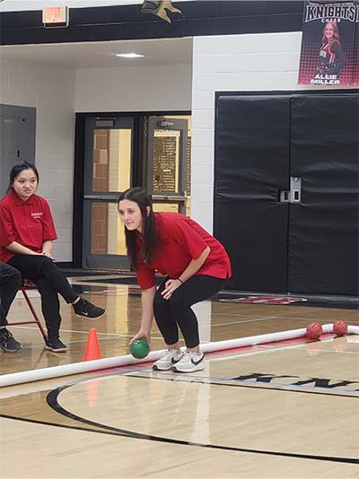 female student rolling a green bocce ball